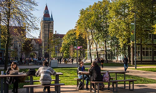 Students sitting on a bench in Brunswick Park on The University of Manchester campus